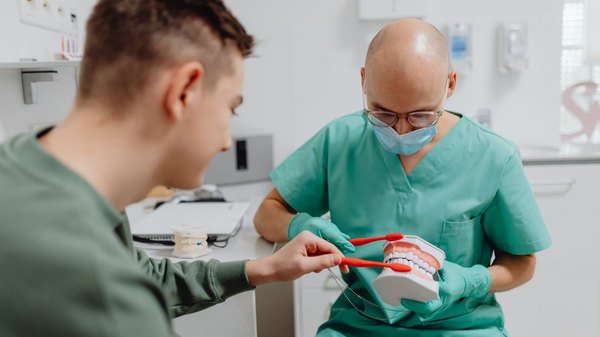 Cirurgião-dentista demonstrando a técnica de escovação em um modelo de arcada dentária