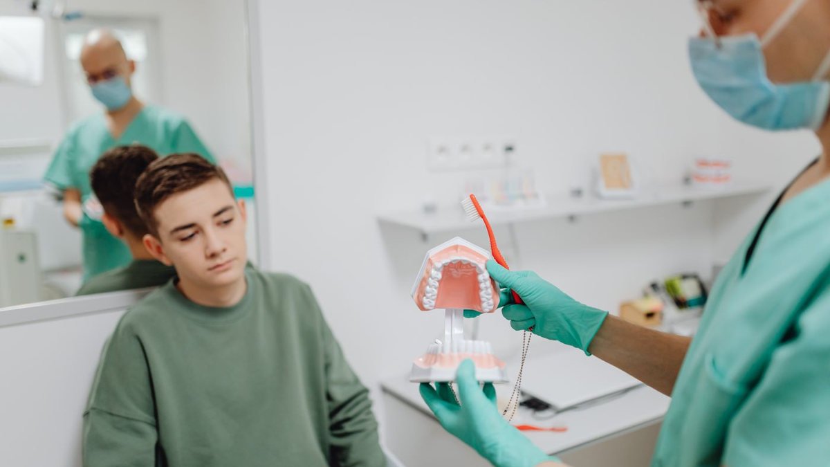 Cirurgião-dentista explicando a um paciente usando um modelo de arcada dentária