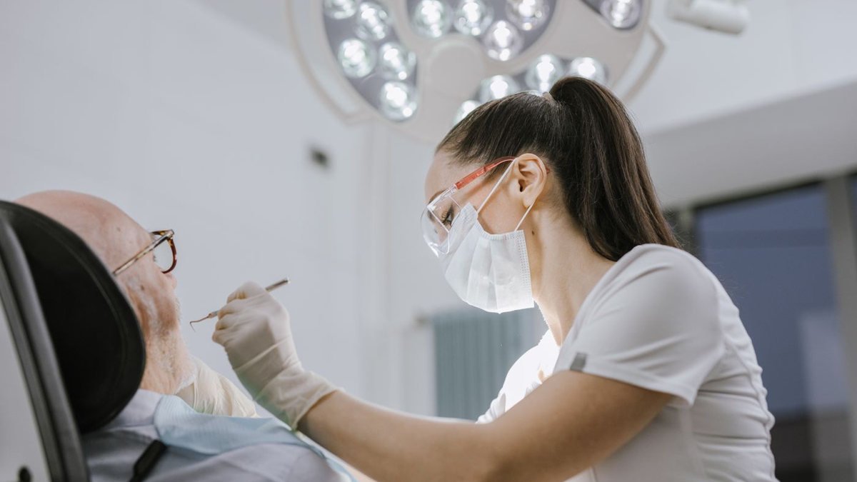 Cirurgiã-dentista examinando os dentes de um paciente sob o refletor odontológico